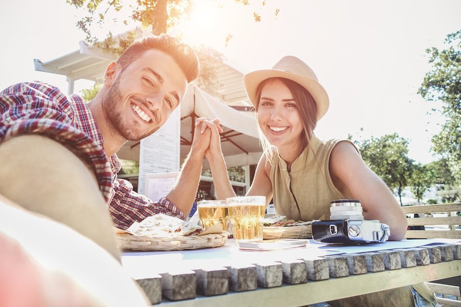 Handsome couple taking selfie with mobile smart phone camera - Young fashion tourist making photo souvenir while eating meal at bar street food restaurant - Vacation and love concept - Warm filter