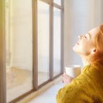 schöne frau genießt die sonnenstrahlen am fenster