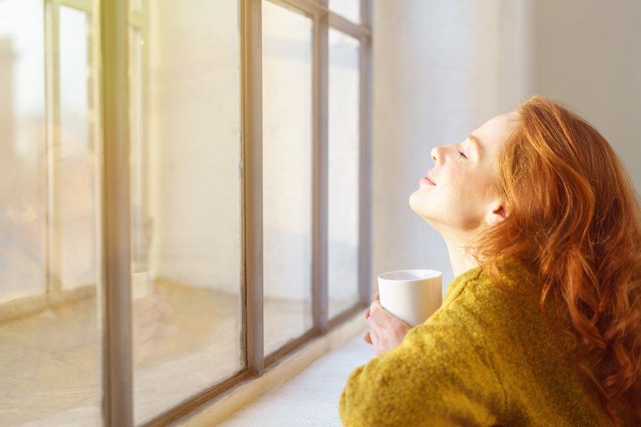 schöne frau genießt die sonnenstrahlen am fenster