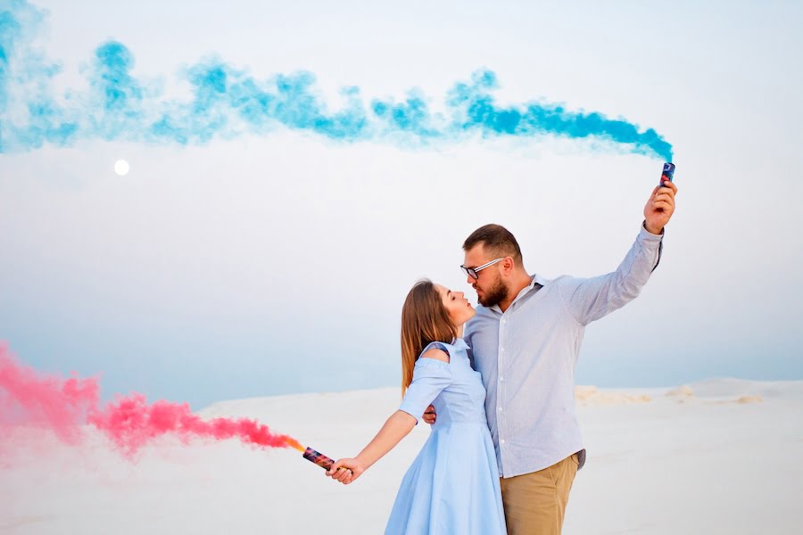 young couple  standing on a sand and holding smoke bomb and looking at each other, romantic couple with blue color and red color smoke bomb on beach