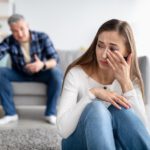 Emotional or psychological domestic violence concept. Mature man abusing his depressed wife, shouting, humiliating and threatening her, middle aged woman crying on floor at home