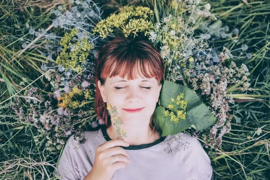 Lächelnde Frau liegt in einer bunten Blumenwiese und blickt in den Himmel