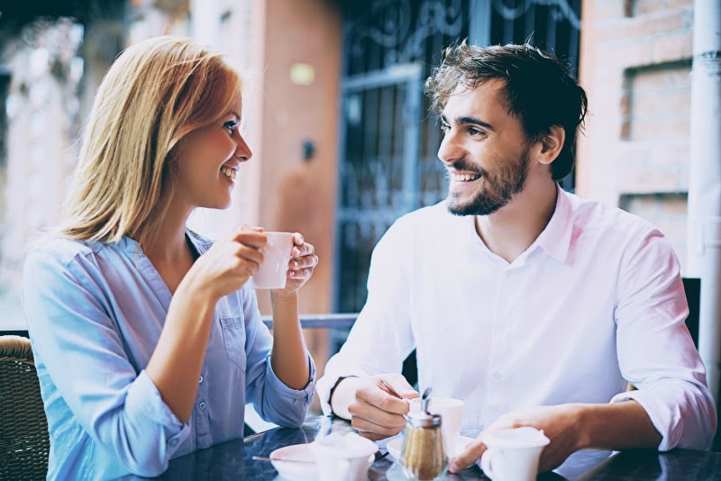 Ein glückliches Paar sitzt in einem Café, trinkt gemeinsam Kaffee und lächelt sich liebevoll an, während sie miteinander sprechen.