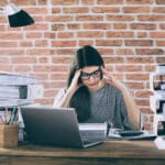 Gestresste Frau im Büro, überfordert von Aufgaben – typisches Beispiel für People Pleasing und das Problem, nicht Nein sagen zu können im Berufsalltag