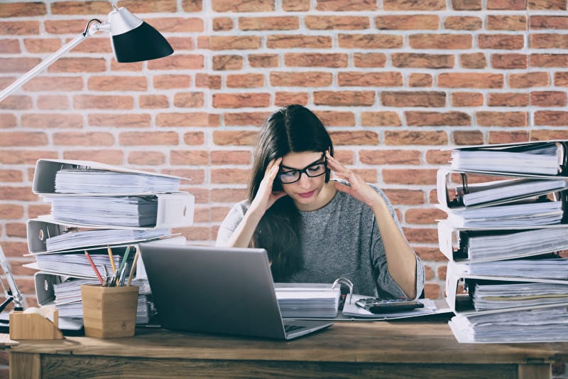 Gestresste Frau im Büro, überfordert von Aufgaben – typisches Beispiel für People Pleasing und das Problem, nicht Nein sagen zu können im Berufsalltag
