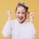 Junge blonde Frau jubelt vor Freude, mit einem strahlenden Lächeln im Gesicht