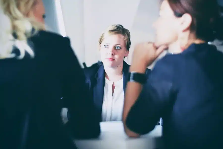 Drei Frauen, von denen zwei den Rücken zeigen, während eine ernst in die Kamera blickt