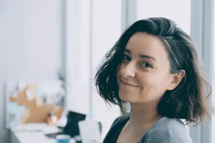 Lächelnde Frau mit halblangen dunklen Haaren im modernen Büro – authentisches Porträt für Coaching, Persönlichkeitsentwicklung und Selbstreflexion