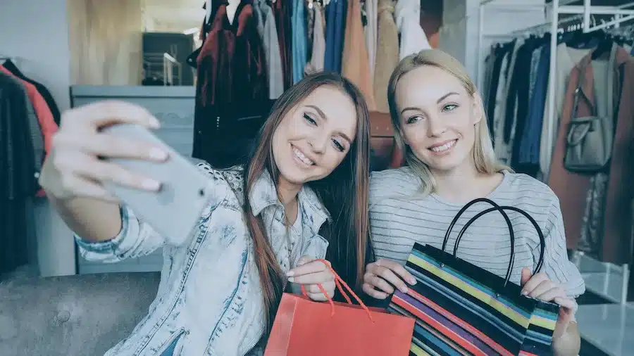 Zwei junge Frauen in einem Bekleidungsladen, die zusammen ein Selfie machen und lachen