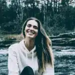 Strahlende Frau mit langen braunen Haaren vor einem Fluss in der grünen Natur