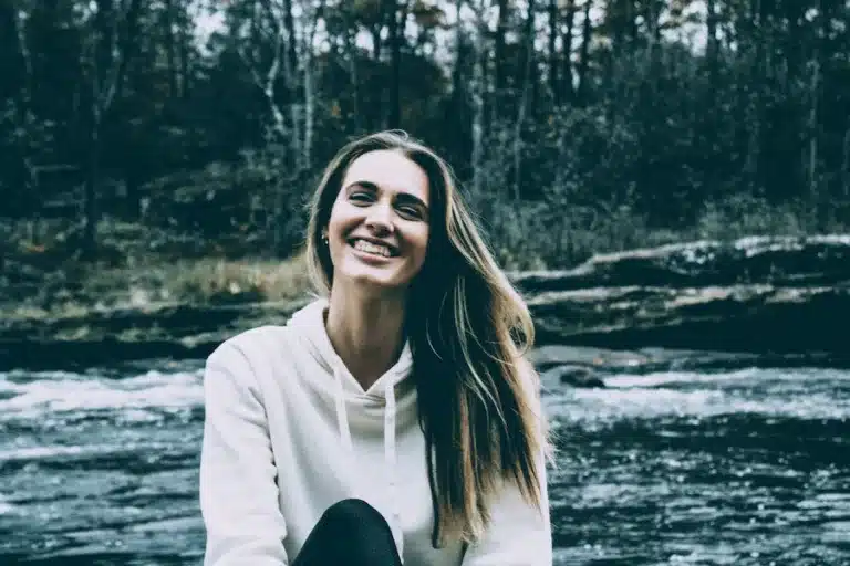 Strahlende Frau mit langen braunen Haaren vor einem Fluss in der grünen Natur