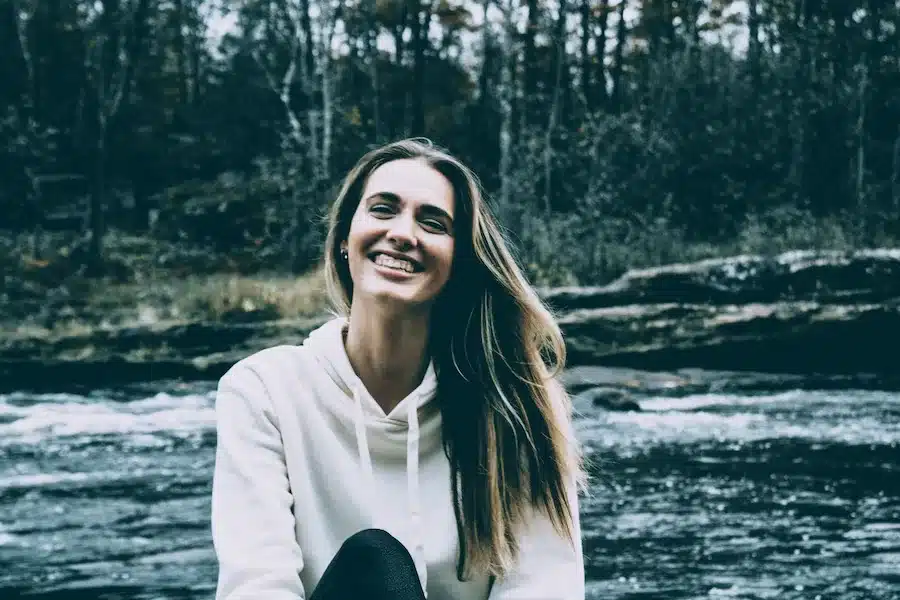 Strahlende Frau mit langen braunen Haaren vor einem Fluss in der grünen Natur